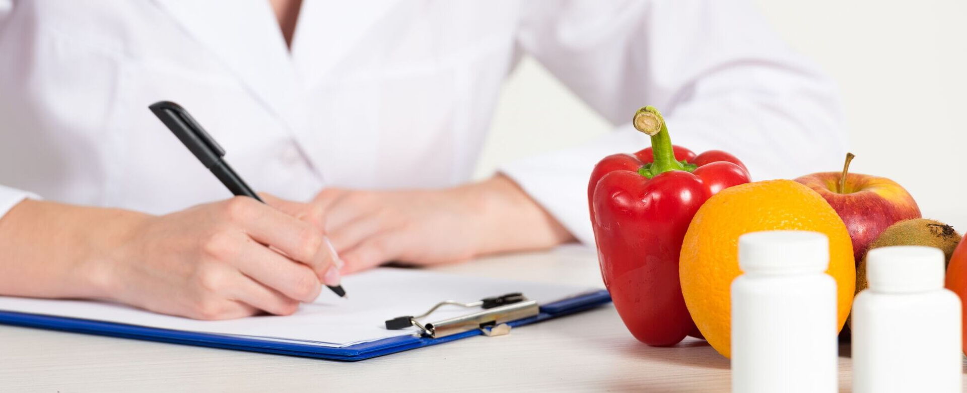 Eine Ernährungsberaterin notiert gesunde Tipps zur Diabetologie mit frischen Früchten und Gemüse auf einem Tisch.